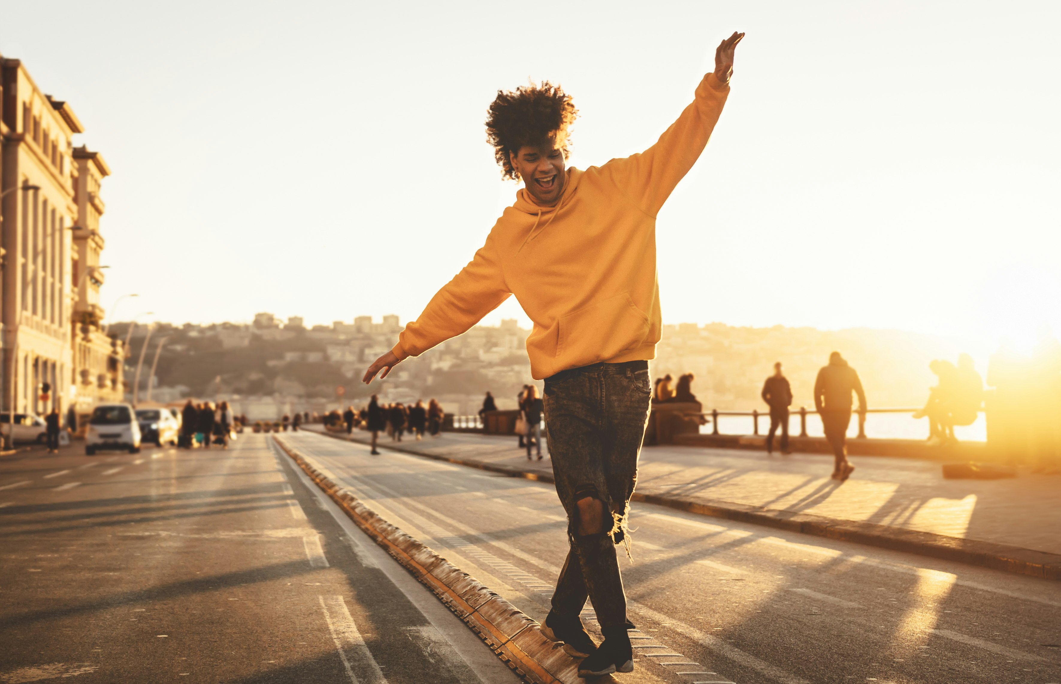 A smiling young man walks at sunset down the median of a waterfront street in Naples